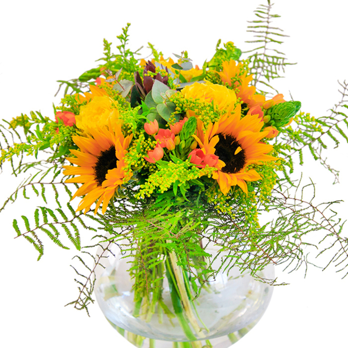 An exuberant bouquet, inspired by the beauty of Hampton's leafy gardens, fills a clear, rounded vase with a cascade of color and texture that captures the delight of late summer gatherings. Radiant sunflowers dominate the display, their burnished golden petals and bold brown centres echoing the warmth of the afternoon sun seen over Hampton Green. Closely grouped buttery-yellow roses add a timeless essence, each bloom finely layered and gently unfurling as if sharing their secrets. Punctuating the landscape, bright red hypericum berries dance across the foliage, adding glossy contrast and playful energy reminiscent of the vibrant Saturday markets on Station Road. Wispy, soft ferns arch gracefully around the arrangement's edge, enriched by ethereal sprigs of goldenrod and slender green spikes, creating a dynamic sense of life and movement. Bluish eucalyptus leaves interlace delicately among the greenery, providing cool highlights that elevate the overall design and call to mind the garden paths near the Thames. The bouquet's natural architecture is accentuated by the sparkling clarity of its glass vase, which nestles each stem in fresh water, enhancing the bouquet's sense of immediacy and freshness. Gentle, uplifting notes of rose perfume blend with the earthy scent of foliage, conjuring memories of open-air picnics and laughter with friends in Hampton. Ideal for celebratory occasions-birthdays, anniversaries, or simply bringing happiness to a loved one's day-this arrangement demonstrates Flowers Hampton's passion for enduring beauty and local artistry. It is a joyful invitation to savour every moment, delivered from the heart of Hampton.